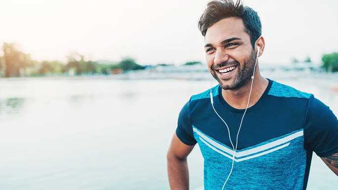 Smiling young man listening to music enjoying outdoor exercise
