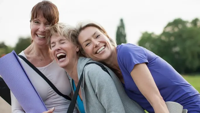 Three female friends laughing after an outdoor yoga class