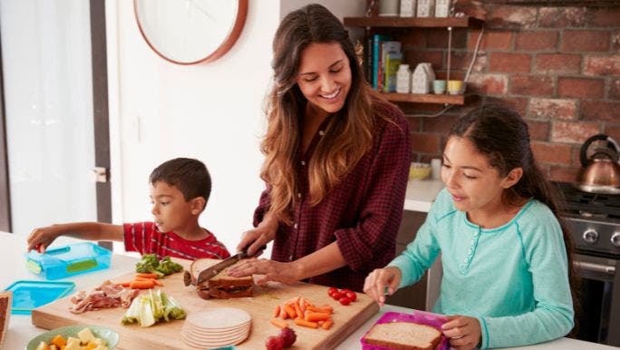 A young mother is preparing healthy food in a kitchen with her two young children