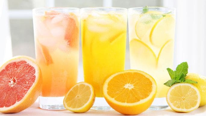 Three glasses of fresh juice are displayed on a table with oranges, lemons and a grapefruit sliced open on the table