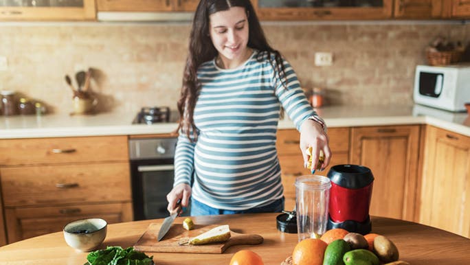 A pregnant woman in a striped top is making a smoothie using fruit like bananas, which may assist gut health