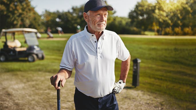 A senior man wearing a white shirt and a cap is playing golf