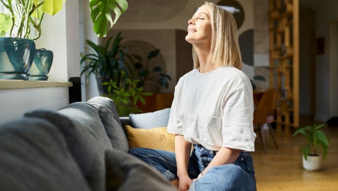 A young woman is sitting cross-legged in front of a window practising breathing exercises 