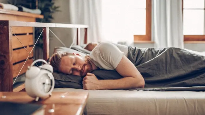 Young man in bed late for work with alarm clock ringing