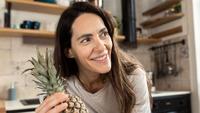 A young woman is smiling and holding a pineapple