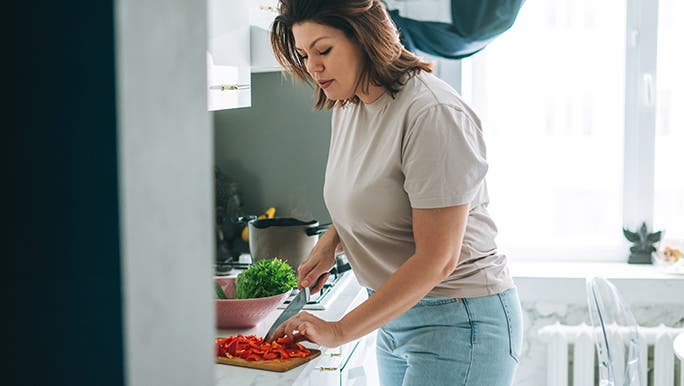 A woman cuts vegetables in her kitchen, she is exploring the benefits of fermented foods. 