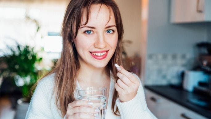 A young woman is smiling and holding a glass of water as she takes a probiotic for immunity