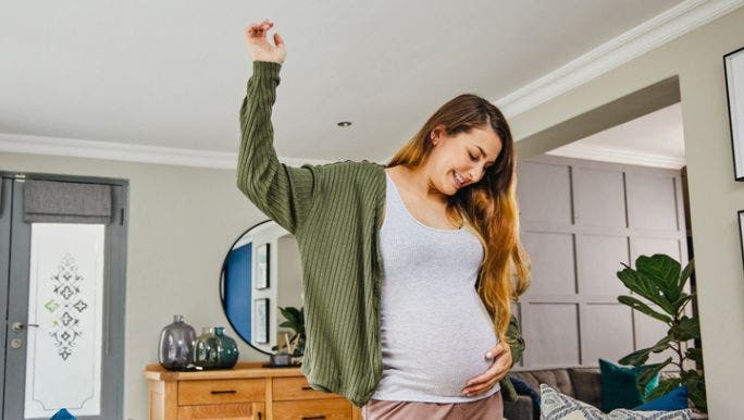 A young pregnant woman is smiling and holding her belly as she looks down