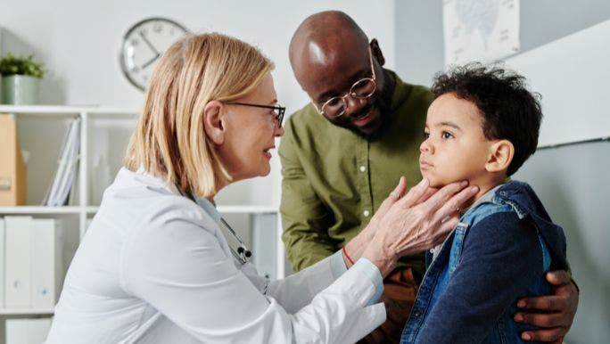 A female doctor is examining a young sick boy as his father looks on