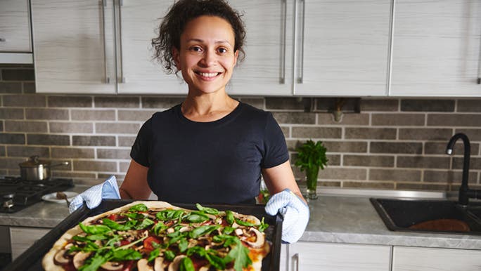 A woman has just taken a vegan pizza out of the oven which is part of her vegan nutrition plan. 