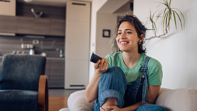 A woman is sitting on the couch with a remote in her hand. She is having a rest day / day off. 