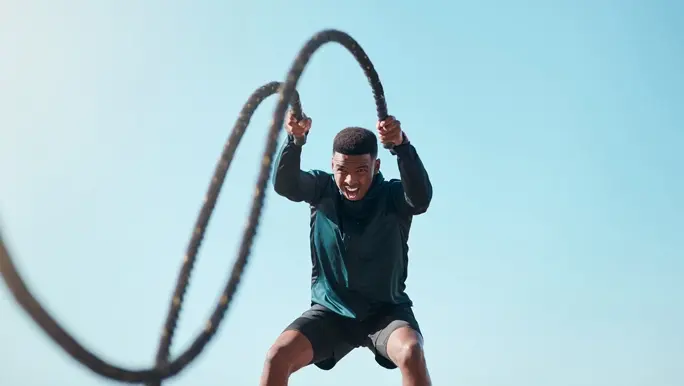Man in black active wear doing a H.I.I.T workout with battle ropes