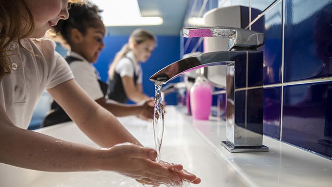 Three children wash their hands in a school bathroom.