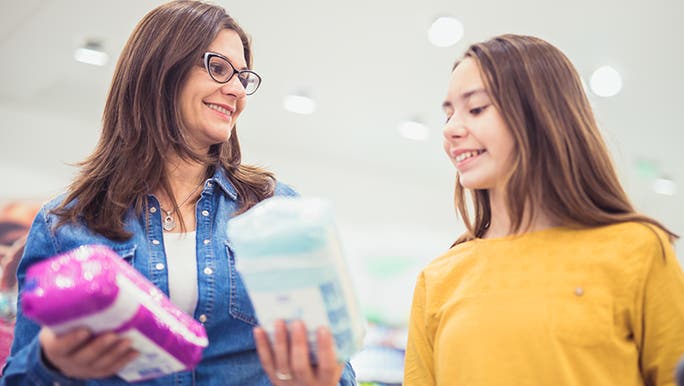 Female caregiver showing a teenager two packets of sanitary products in the supermarket. They are discussing the signs that your first period is coming. 
