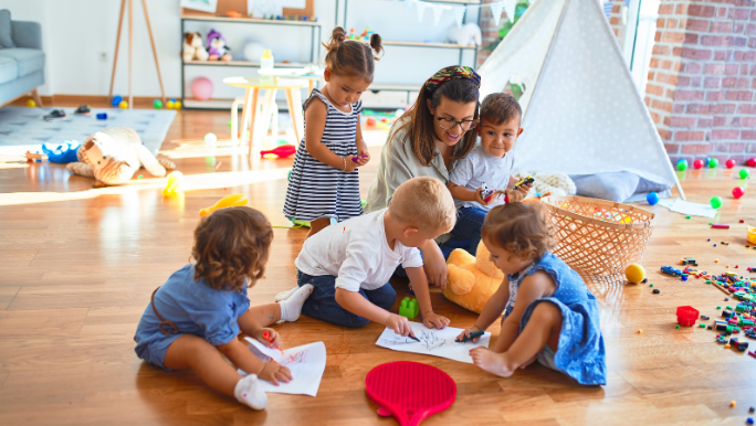 A group of toddlers are playing on the floor with their teacher in a daycare centre