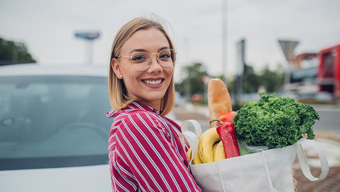 Holding her shopping in a reusable bag, a woman looks happy because she bought vegetables in season in Australia. 