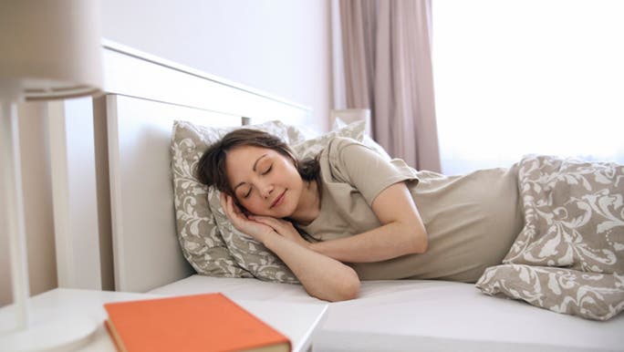 A woman with dark hair is sleeping on her side in a bright bedroom