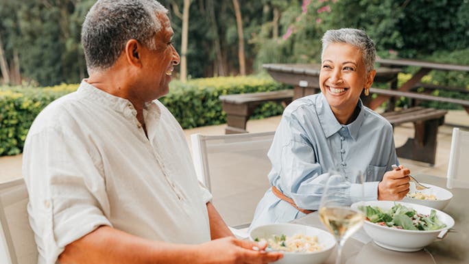 An older couple looking at each other and smiling as they eat salad