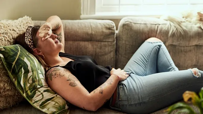 Woman with abdominal cramps lying on the couch at home