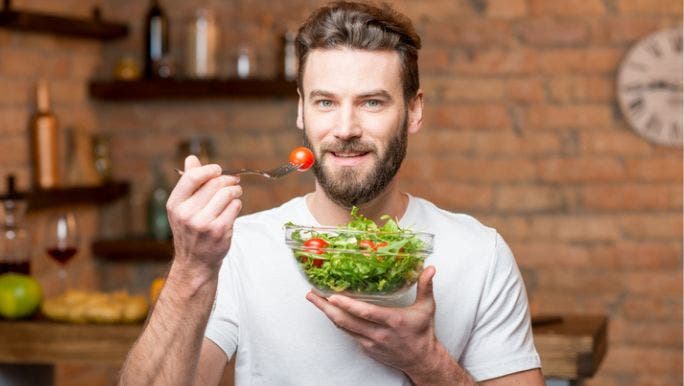 A young man is smiling at the camera as he eats a salad