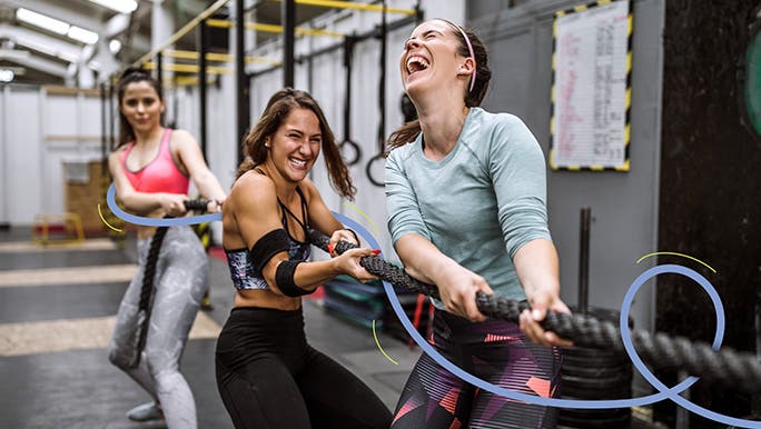Three female friends working out in the gym pulling a combat rope