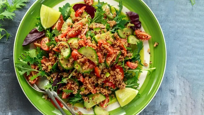 Fresh salad with quinoa, cherry tomato, cucumber, rocket and lime in a green and white bowl