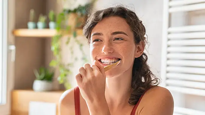 Woman smiles while brushing her teeth in the bathroom.