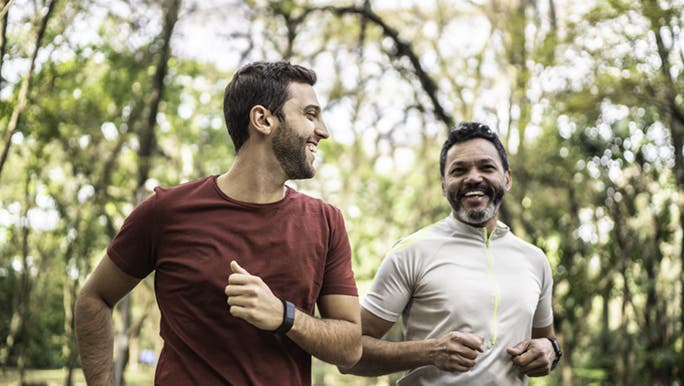 Two men run through a park together, they exercise weekly to stay healthy. 
