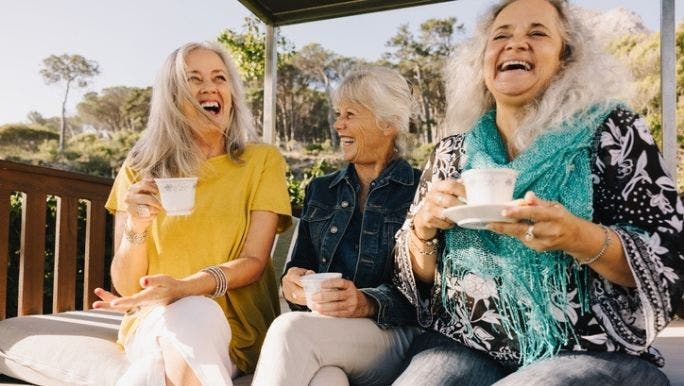 Three senior women are laughing and drinking tea together