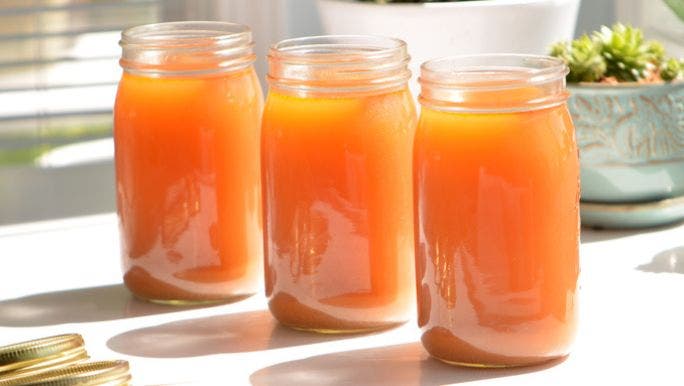 Three glass jars are filled with golden bone broth with pot plants in the background