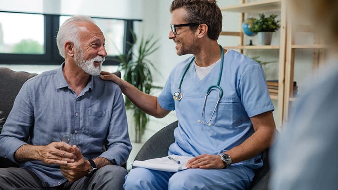 A man over 40 with grey hair and a beard is smiling at a doctor while having a health check
