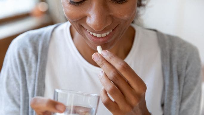 A woman is about to take a supplement with a glass of water