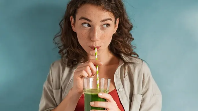 Young woman drinking a green juice through a green and white paper straw