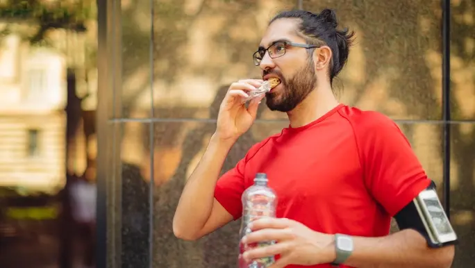 Active man in a red t-shirt snacking on a high fibre muesli bar