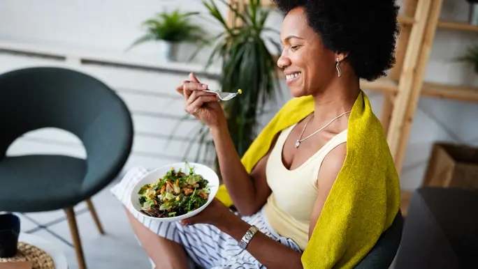 Relaxed and smiling woman eating vegetables at home