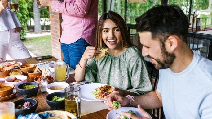 A group of people are gathered around a table eating Mexican food containing legumes, which are a good source of prebiotics