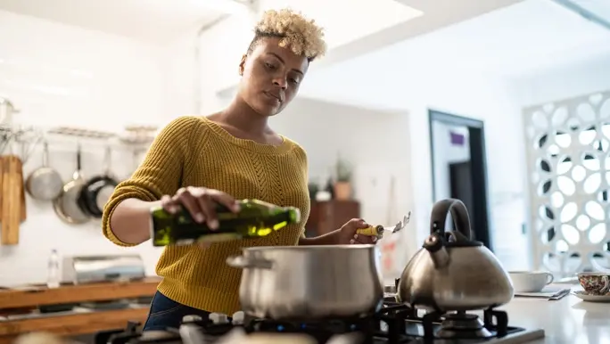 Young woman preparing food at home using extra virgin olive oil