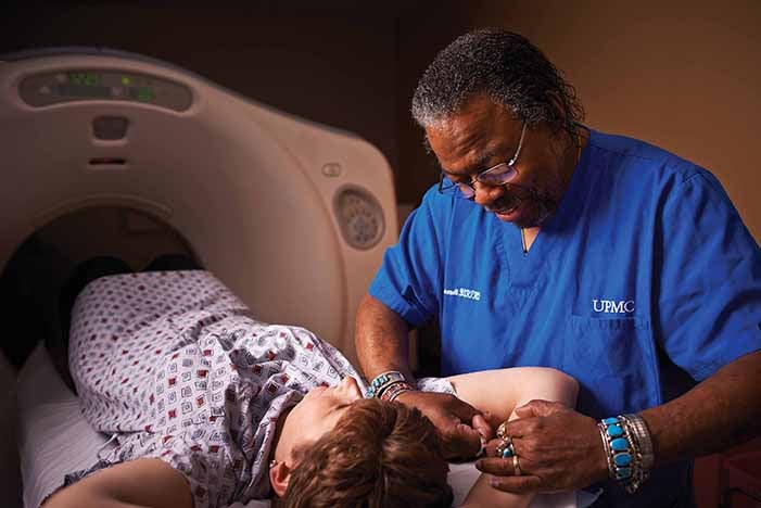 A male R.T. in blue scrubs comforting a patient on a scanner bed
