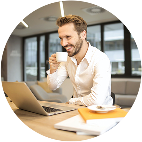 Round photo of a smiling man with light hair and a beard drinking a cup of coffee while looking at his open laptop