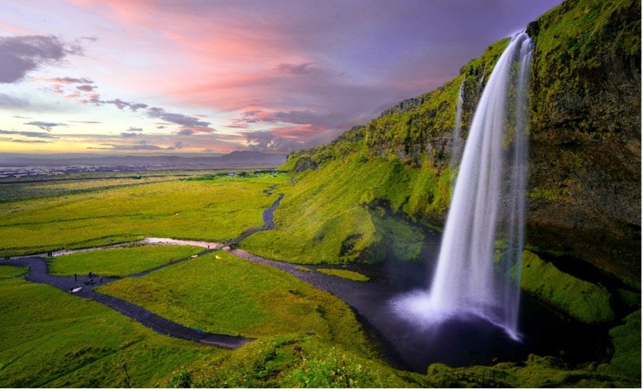 A tall, stunning waterfall flows off of a green mountain at sunset.