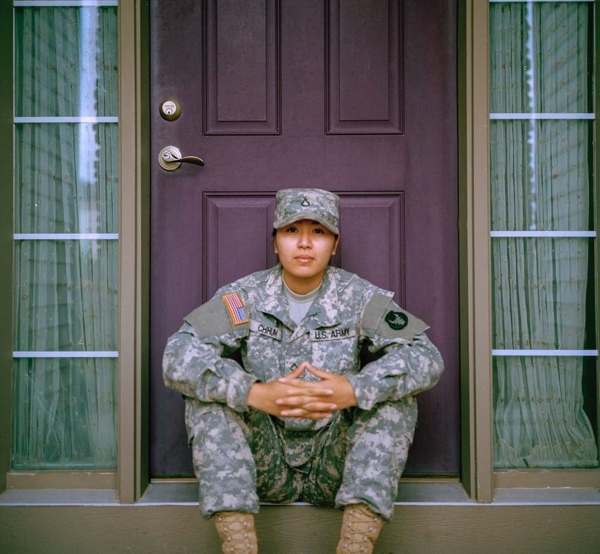 A young woman in military attire sitting on the steps of a house. Behind her is a purple door.