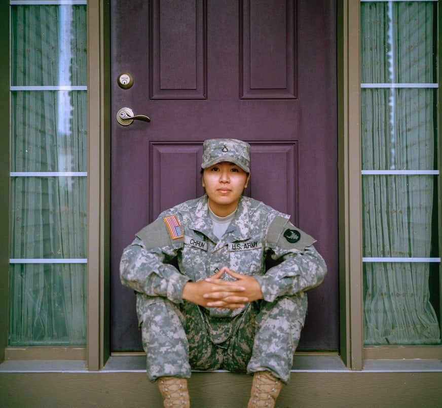 A young woman in military attire sitting on the steps of a house. Behind her is a purple door. A young woman in military attire sitting on the steps of a house. Behind her is a purple door.