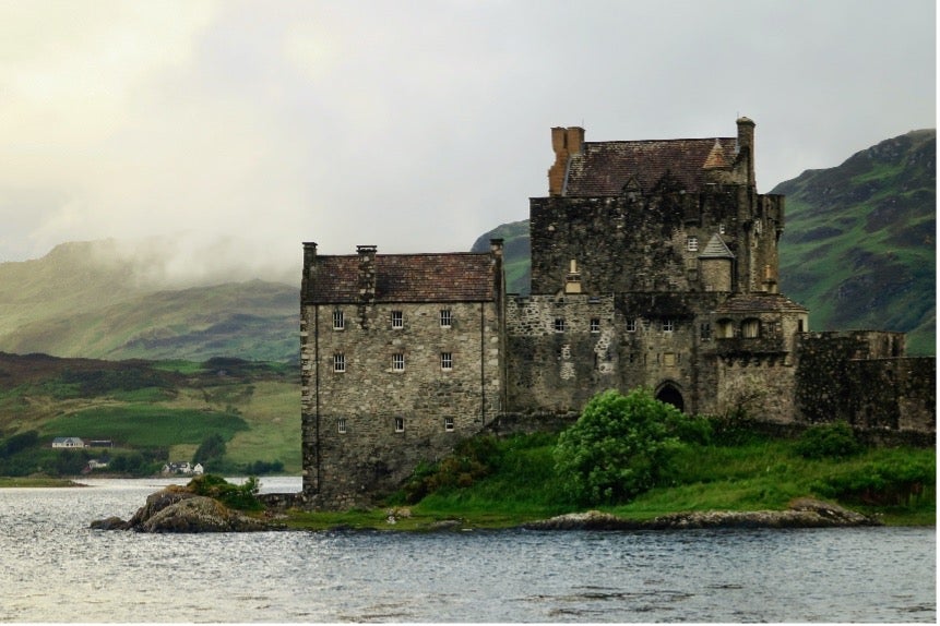 A castle sits on a green stretch of land next to a lake in Dornie, Scotland.