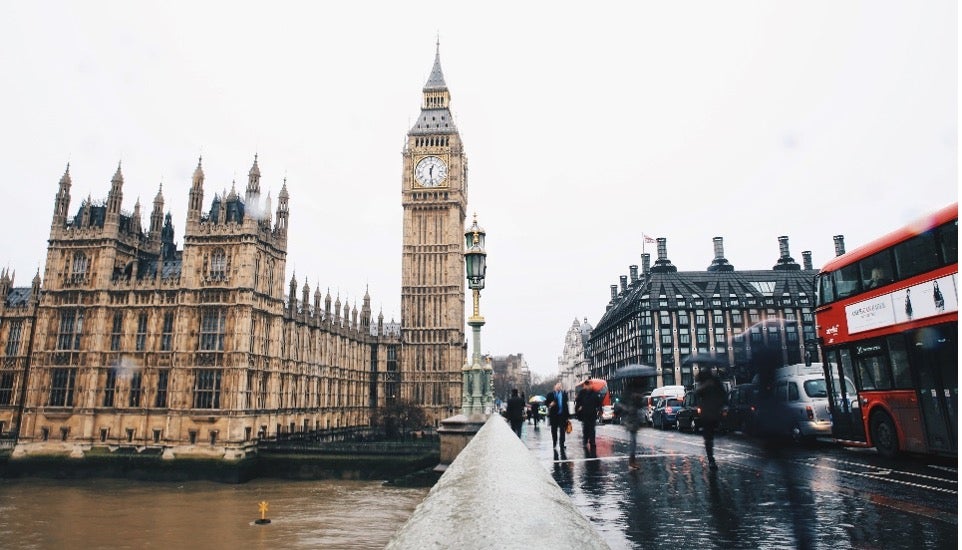 Big Ben’s clock tower stands against a grey sky as a double-decker bus drives by in London, England