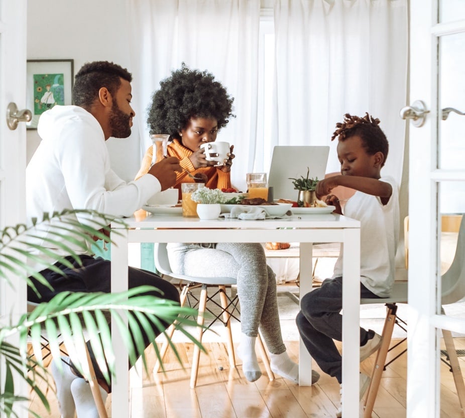 A man, woman, and a child sitting at a table & having a meal together.