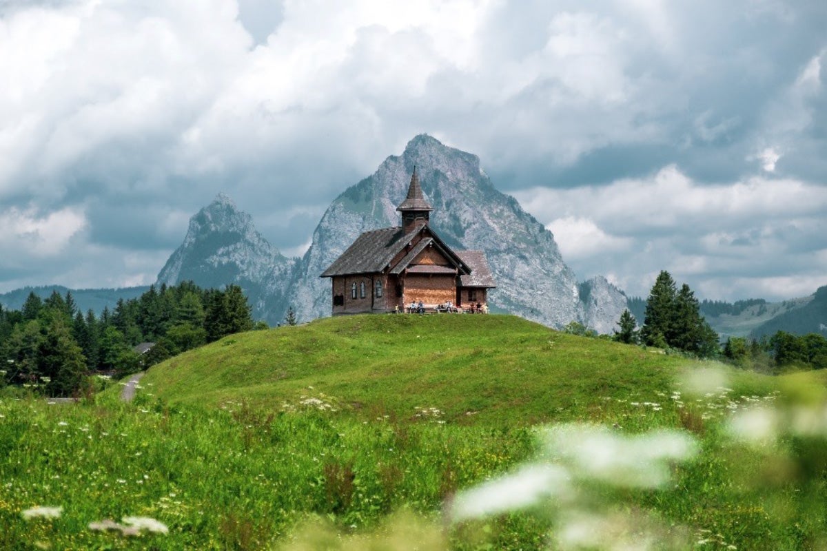 A mountain looms over a small church on a hill in Stoos, Switzerland