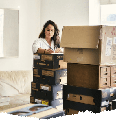 Woman writing on a stack of boxes. There are more boxes in the room as she prepares for relocation. 