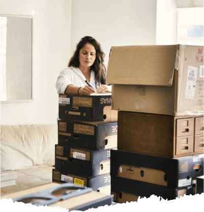 Woman writing on a stack of boxes. There are more boxes in the room as she prepares for relocation. Woman writing on a stack of boxes. There are more boxes in the room as she prepares for relocation.