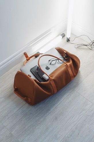 A leather duffel bag sits open revealing a Macbook, glasses, and an iPhone its owner will move to Portugal.