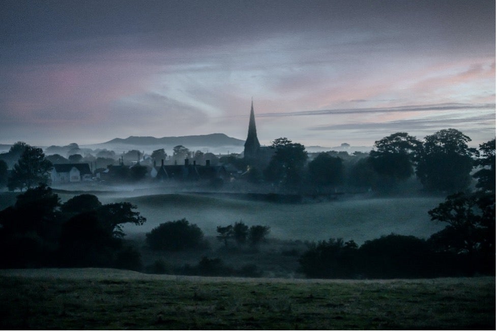 Across a green field, Llandwrog town peeks out of the fog in northern Wales.
